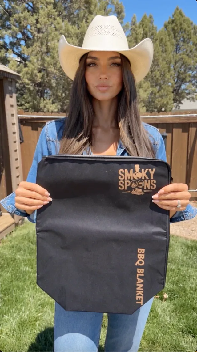 Woman in a cowboy hat holding the Smoky Spoons BBQ Blanket in her backyard